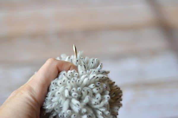 darning needle sewing on a yarn pom-pom 