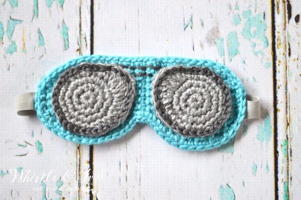 crochet sleep mask that looks like aviator sunglasses on white wood slats