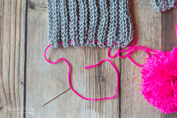 sewing pom-pom to crochet scarf 